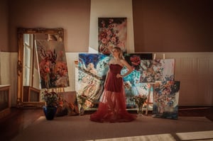 Woman standing in red dress in front of paintings of flowers and women